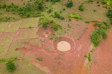 Laos 'taki Plaine des Jarres platosundaki yuvarlak çamurlu göletler ve yamalı yeşil çayırlar için insansız hava aracı perspektifi. Manzara kırmızımsı toprak, dağınık çalılar ve yumuşak gün ışığı altında ince doğal dokulara sahiptir..