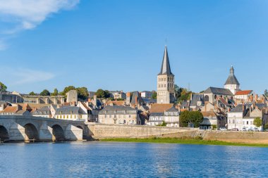 Parlak sabah ışığı, La Charite sur Loire 'ın tarihi ufuk çizgisini aydınlatmakta, taş köprüsü, kilise kulesi ve Loire nehri boyunca geleneksel evleri ile. Açık mavi gökyüzü ve sakin su ortaçağ mimarisi ve nehir kenarını vurguluyor.
