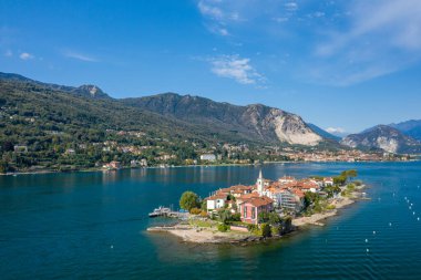 Parlak gün ışığı, Isola dei Pescatori 'nin renkli binalarını, kilise kulesini ve kıyı şeridini, derin mavi sularla çevrili ve orman tepeleri ve engebeli dağlarla desteklenmiş. Huzurlu ada sahnesi kuzey İtalya 'daki Maggiore Gölü' nde yer alıyor.