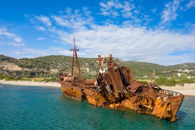 Dimitrios 'un gemi enkazı, Yunanistan' ın Gythio kentindeki parlak mavi gökyüzünün altında yeşil tepeler ve dağınık evler tarafından desteklenen kumlu bir sahil yakınındaki sığ turkuaz sularda ağır paslanmış ve kırılmış bir halde yatıyor..
