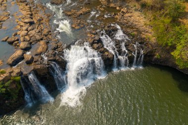 Tad Lo şelalesinin engebeli kayaların üzerinden akan sular güney Laos 'taki geniş bir havuza akarken geniş bir hava perspektifi. Güneş ışığı dokuları akan su, açıkta kalan taş ve çevreleyen yeşillik arasındaki zıtlığı vurgular..