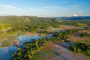 Hava perspektifi, taşkın pirinç tarlalarının, kırsal alanda geometrik desenler oluşturduğunu, köy evleri kümelerinin ve yoğun yeşilliklerin dramatik kireçtaşı tepelerine kurulduğunu ortaya koyuyor. Sabahın erken saatlerinde güneş ışığı yansıtıcı suyu vurgular.