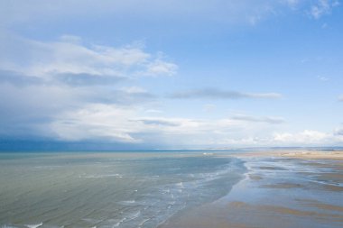 Ouistreham 'daki Kılıç Sahili' nin geniş manzarası yumuşak dalgalarla dolu dramatik bir gökyüzü altında geniş gel-git kumlarıyla buluşuyor..