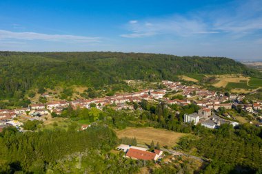 Saint-Maurice-sous-les-Cotes 'un havadan görünüşü yoğun ormanlık bir tepenin dibinde, kırmızı kiremitli çatılar, açık alanlar ve açık mavi gökyüzü altında yeşil yaz bitkileri. Sahne, geleneksel kırsal evlerin yamasını vurguluyor.