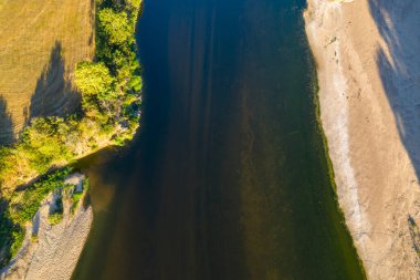 Loire nehrinin temiz su ve güneş ışığı dokularıyla geniş bir kumlu sahil ve yeşil bitki örtüsüyle çevrili havadan bakış açısı. Yazın kırsal bir nehir manzarasının doğal desenlerini ve zıt renklerini vurgular..