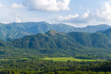 Yoğun bir orman ve canlı pirinç tarlalarıyla dolu geniş bir vadi manzarası var. Kuzey Vietnam 'da dağınık bulutlarla kaplı bir gökyüzünün altındaki katmanlı mavi dağlara karşı kurulmuş. Manzara açık, huzurlu ve doğal olarak zengin hissettiriyor..