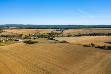 Hava perspektifi, Fransa 'nın merkezinde, geniş altın tarlalar, dağınık ağaçlar ve açık mavi gökyüzünün altındaki uzak ormanlık alanlarla çevrili bir kırsal köyü ortaya çıkarıyor. Açık tarım arazileri ve nazik tepeler ferah ve kırsal bir sükunet hissi yaratıyor.