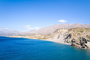 Parlak güneş ışığı, Girit 'in güney kıyıları boyunca uzanan kayalık uçurumlar ve kurak yamaçlarla çevrili ve berrak gökyüzünün altında uzanan derin mavi Akdeniz sularını aydınlatır..