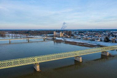 Loire Nehri 'ni geçen soluk yeşil bir demir köprü tarihi Sully sur Loire kalesi ve arka planda kar kaplı çatıları ile soğuk bir kış gökyüzünün altında görünür..