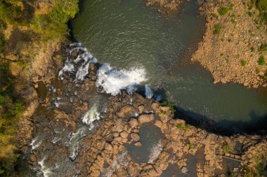 Tepetaklak bir perspektif, Tad Lo şelalesinin engebeli kayaların üzerinden akan suları, dağınık kayalar ve güney Laos 'taki seyrek yeşilliklerle çevrili sakin bir havuza yansıtıyor. Güneş ışığı, dokulu taşları ve yumuşak akışı vurgular, huzur uyandırır.