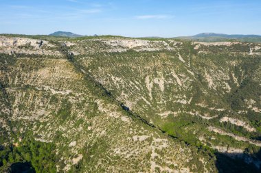 Navacelles Sirki 'nin dağınık yeşillikleriyle kaplı engebeli kireçtaşı kanyon duvarlarının geniş manzarası. Güneşli uçurumlar ve derin gölgeler berrak bir gökyüzünün altında dramatik doğal hatları ortaya çıkarıyor..