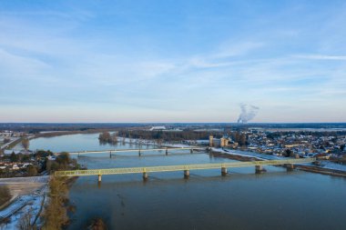 İki köprü Sully sur Loire yakınlarındaki geniş Loire Nehri boyunca uzanır, tarihi bir şato ve soluk bir kış gökyüzünün altında karla kaplanmış bir köy. Manzara sakin, yumuşak ışık ve sakin su, sakin atmosferi yansıtıyor..