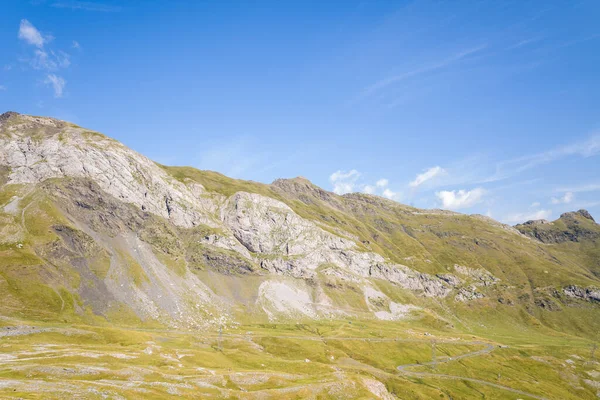 Gavarnie Gedre yakınlarındaki Pireneler 'de berrak bir mavi gökyüzünün altında çıplak kaya oluşumları ve çimenli yamaları olan güneşli bir dağ yamacının geniş manzarası. Manzara yumuşak yükseklik ve doğal toprak tonlarına sahiptir..