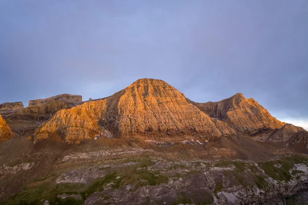 Yumuşak günbatımı ışığı Pireneler 'deki önemli bir dağ sırasının engebeli, çizgili kaya oluşumlarını yıkıyor, sakin bir akşam gökyüzünün altında sıcak dokuları vurguluyor..