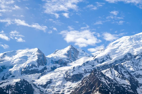 Kıtır güneş ışığı Mont Maudit 'in engebeli, karla kaplı zirvelerini aydınlatmakta açık bulutlarla dağılmış parlak mavi gökyüzü, keskin dokular ve dramatik alp formları..