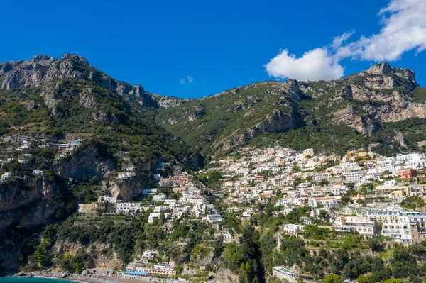 Positano, İtalya 'nın beyaz ve pastel binaları engebeli kireçtaşı dağlarının altında sarp yeşil yamaçlar boyunca kurulmuştur. İkonik Amalfi Sahil Köyü, gür bitki örtüsü ve dramatik uçurumların çerçevelediği canlı mavi gökyüzüne karşı kurulmuştur.