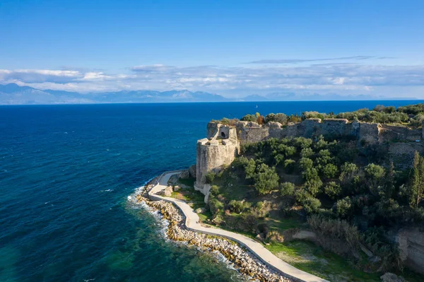 Yunanistan 'ın Koroni kenti yakınlarındaki parlak bir gökyüzü altında, yemyeşil zeytinlikler ve dolambaçlı bir kıyı yolu ile çevrili, derin mavi Akdeniz' e bakan antik taş surlar görülüyor..
