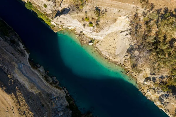 Corinth Kanalı 'nın yukarıdan aşağıya canlı turkuaz su, dik kireçtaşı uçurumları ve seyrek bitki örtüsüyle benekli, kurak, güneşli arazi görüntüsü..