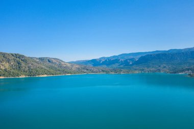 Sainte-Croix gölünün engin manzarası berrak turkuaz su ve bulutsuz mavi gökyüzü altında engebeli dağlar..