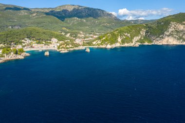 Yunanistan 'ın Epirus kentindeki Parga' nın hava manzarası kayalık uçurumlar, turkuaz su ve yemyeşil tepelerle çevrili renkli bir sahil köyünü gösteriyor. İyon kıyı şeridi ve dağlık zemin açık gün ışığında canlı bir Akdeniz manzarası yaratır..