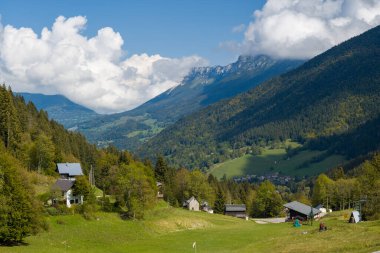 Dağılmış kırsal evler yeşil çayırlar ve Chartreuse Massif 'in yamaçlarında yoğun ormanlar arasında yuva yapar, çarpıcı zirveleri ve canlı mavi gökyüzünün altında dalgalanan bulutları vardır. Sahne, bu simgenin gür dokularını ve sakin atmosferini yakalıyor.