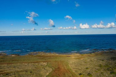 Adriyatik Denizi 'nin geniş manzarası dağınık bulutlarla kaplı canlı mavi bir gökyüzü altında kayalık bir kıyı şeridi ve çimenli bir araziyle kesişiyor. Sahne, güney İtalya 'da açık kıyı alanları, yumuşak dalgalar ve doğal dokuları yakalıyor..