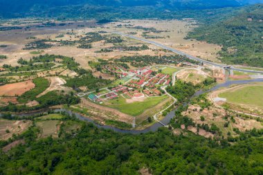 Kırmızı çatılı binaları olan planlanan bir köy, dolambaçlı bir nehrin kenarında, yama alanları, orman ve uzak tepelerle çevrili. Manzarada geometrik planlar, ekili arazi ve açık kırsal alanlar açık gün ışığı altında yer almaktadır..