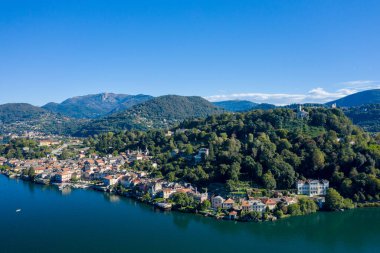 Orta San Giulio 'nun hava perspektifi kuzey İtalya' daki Orta Gölü kıyıları boyunca uzanır ve göl kenti arkasında yemyeşil ağaçlık tepeler yükselir. Sahnede berrak mavi su, dağınık villalar ve dingin bir hava var.