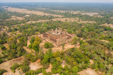 Kamboçya 'nın Angkor bölgesindeki kuru tarlalar, dağınık ağaçlar ve uzak su rezervleriyle çevrili antik Pre Rup tapınağı kompleksinin geniş hava perspektifi. Sahne, kırsal alandaki tapınakların geometrik düzenini yakalıyor.