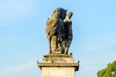 Paris 'te Pont de Iena' daki bir kaidede bir adam ve bir atı tasvir eden klasik taş heykel, açık mavi gökyüzüne karşı sıcak güneş ışığıyla aydınlatılıyor..