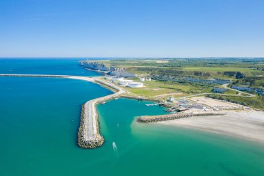 Kıvrımlı dalgalı suları, turkuaz suyu, beyaz depolama tankları ve Normandiya kıyı şeridi boyunca uzanan dramatik uçurumları olan liman girişi berrak mavi bir gökyüzünün altında..