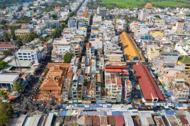 Orta Chau Doc, Vietnam 'daki hareketli pazar alanının hava perspektifi, renkli çatılar, tarihi bir tapınak ve ayırt edici sarı pazar salonu. Görüntü, yoğun şehir bloklarını, hareketli sokak şekillerini ve yeşil pirinç tarlalarını yakalıyor.
