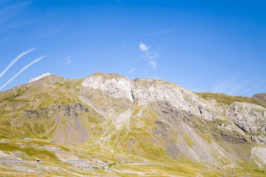 Yeşil çimenli yamaçları ve açık kayalık yüzeyleri olan parlak bir dağ sırtı, Gavarnie Gedre yakınlarındaki Pireneler 'de canlı mavi bir gökyüzüne karşı kurulmuştur. Manzara yumuşak hatlar, doğal dokular ve barışçıl bir açık atmosfere sahiptir..