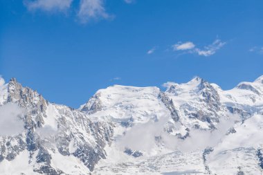 Mont Maudit ve Mont Blanc du Tacul 'un karla kaplı zirveleri sürüklenen bulutların üzerinde yükseliyor, Fransız Alplerinde canlı mavi bir gökyüzüne karşı kuruluyor..