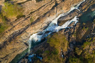 Hava perspektifi, Champasak Eyaleti 'ndeki Li Phi Şelaleleri olarak da bilinen Tat Somphamit Şelaleleri' ndeki engebeli kayalık vadiyi ve çağlayan suyu aydınlatan sabah güneşini gösteriyor. Korunmasız taş, kıvrılan akıntılar ve seyrek kurak orman.