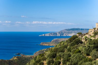 Taş kalıntıları, Yunanistan 'ın Vathia kenti yakınlarındaki dramatik kıyı kayalıkları ve derin mavi Akdeniz manzaralı yemyeşil bir yamaçta yer alıyor. Sahnede canlı yeşillik, engebeli arazi ve çarpıcı bir doğal manzara için açık gökyüzü yer alıyor..