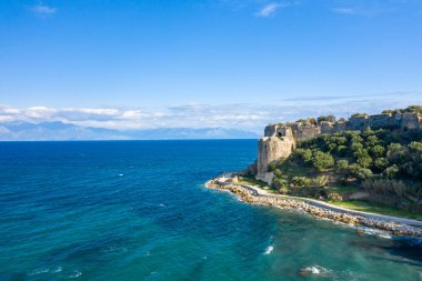 Yunanistan 'ın Koroni kenti yakınlarındaki uzak dağ manzaralı canlı turkuaz sulara tepeden bakan kayalık bir kıyı şeridinin ve yemyeşil yemyeşil suların üzerinde antik kale duvarları yükseliyor..