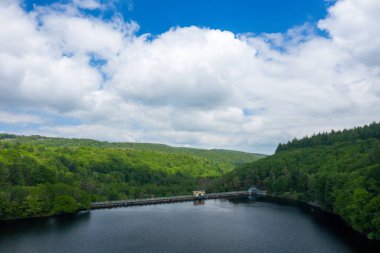 Karanlık, sakin bir göl boyunca uzanan uzun bir baraj yoğun yeşil ormanlarla çevrili ve Chaumecon gölünde büyük, dalgalı bulutlarla dolu bir gökyüzünün altında yuvarlanan tepeler..