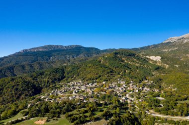 Gökyüzü perspektifi, Yunanistan 'ın Epirus kentindeki sık yeşil ormanlar ve kayan tepeler arasında yuva yapmış Papingo köyünün taş yapılmış evlerini yakalıyor. Parlak güneş ışığı ve parlak mavi gökyüzü Pindus Dağları 'nın katmanlı dokularını ve doğal hatlarını güçlendirir.