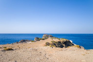 Kuru, kayalık burunlar Girit 'in güney kıyısındaki Agios Pavlos yakınlarında açık bir gökyüzünün altında derin mavi Akdeniz' e çıkar. İnce bitki örtüsü ve engebeli dokular vahşi ve açık bir alanı çağrıştırıyor..