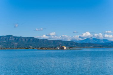 Yunanistan 'ın batısındaki Missolonghi tuz gölünde dar bir arazi şeridi üzerinde sarı çatılı, ıssız taştan bir kilise duruyor. Sakin mavi sular, uzak dağ sırtları ve berrak gün ışığında dağılmış bulutlar barışçıl ve geniş bir sulak arazi yaratır.