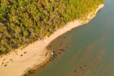 Üst perspektifte yoğun yeşil orman ve Güney Laos 'un Champasak Eyaleti Hang Khon' daki Mekong Nehri 'nin sakin suları ile çevrili sakin bir kıyı şeridi görülüyor. Geleneksel ahşap tekneler plajda dinlenir, sükuneti ön plana çıkarırlar.