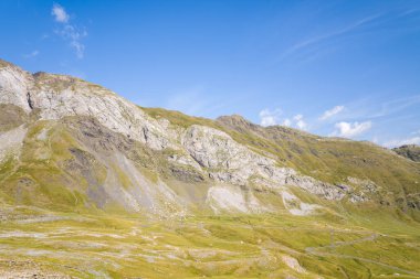 Parlak güneş ışığı, Gavarnie Gedre yakınlarındaki Pireneler 'de parlak mavi gökyüzünün altında engebeli kayalık çıkıntıları ve otlak alp yamaçlarını aydınlatır. Manzara yumuşak kıvrımlar, doğal dokular ve açık dağ arazisine sahiptir..