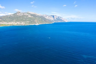 Derin mavi Akdeniz 'in geniş hava manzarası Sardunya' nın Lotzorai yakınlarındaki engebeli yeşil dağlar ve kıyı şeridi ile buluşuyor. Sahne berrak bir gökyüzü ve ince dalgalarla aydınlık ve sakin..