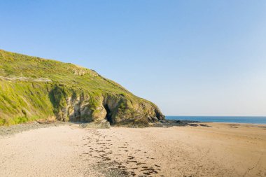 Cap de Carteret, Normandiya 'daki geniş ve ıssız bir kumsal üzerinde yeşil kayalıklar yükseliyor. Sahil şeridi berrak güneş ışığıyla yıkanmış, doğal dokular ve sakin, açık deniz manzarası ortaya çıkmış..