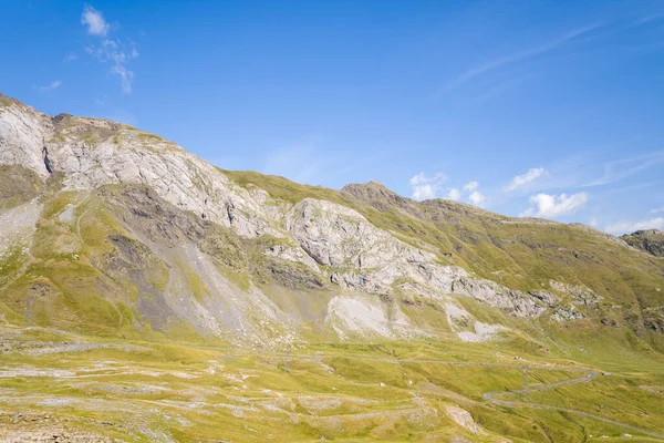 Parlak güneş ışığı, Gavarnie Gedre yakınlarındaki Pireneler 'de parlak mavi gökyüzünün altında engebeli kayalık çıkıntıları ve otlak alp yamaçlarını aydınlatır. Manzara yumuşak kıvrımlar, doğal dokular ve açık dağ arazisine sahiptir..