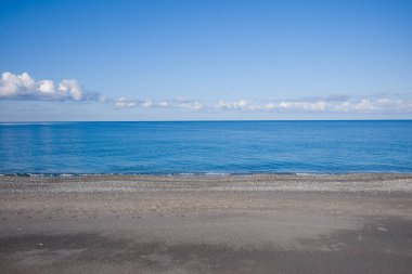 Plage de Acchio, Fiumicello 'daki kumlu ve çakıl taşlı plajlar, bulutların dağıldığı açık bir gökyüzünün altında sakin bir mavi denizle buluşuyor. Sahne açık ve huzurlu, huzurlu bir yalnızlık hissi uyandırıyor..