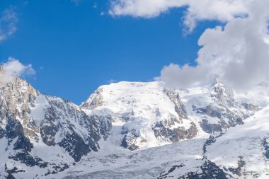 Karla kaplı görkemli yamaçlar ve Mont Blanc du Tacul 'un sarp kayalık tepeleri Fransız Alplerinde dağınık bulutlarla mavi bir gökyüzünün altında yükseliyor..