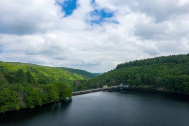 Sakin bir su deposu beton bir barajla çevrilidir ve Lac de Chaumecon 'da dramatik bulutlarla dolu bir gökyüzünün altında yoğun, canlı orman tepeleriyle çevrilidir..