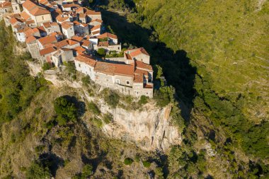 İtalya, Tortora 'da terracotta çatısı olan taştan binaların hava manzarası sarp kayalıklara tünemiş ve sıcak güneş ışığı altında yeşil tepelerle çevrili..